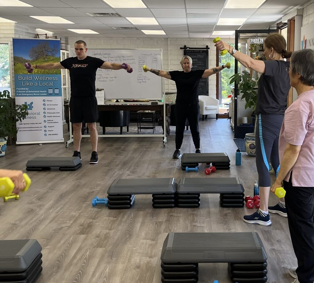 Personal trainer Brian coaching a small group class performing dumbbell lateral raises for shoulder mobility and strength at BeFit.
